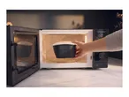A person placing a black collapsible food container into a microwave oven.
