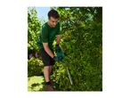 Man in safety glasses and gloves trimming a hedge with a hedge trimmer in a garden.