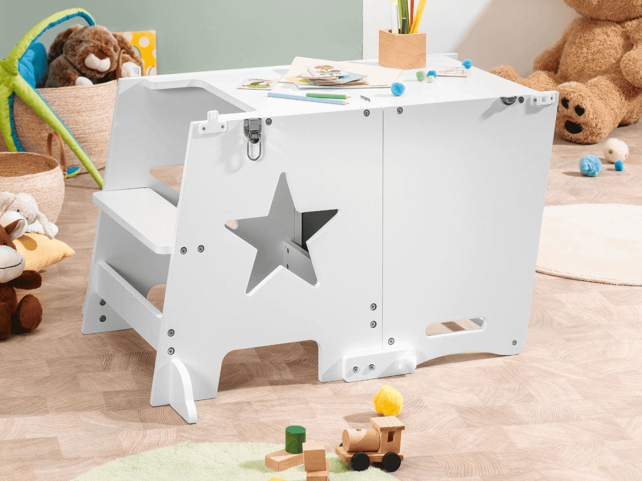 Weißer Lernturm mit Sternausschnitt und Spielzeug auf dem Boden.