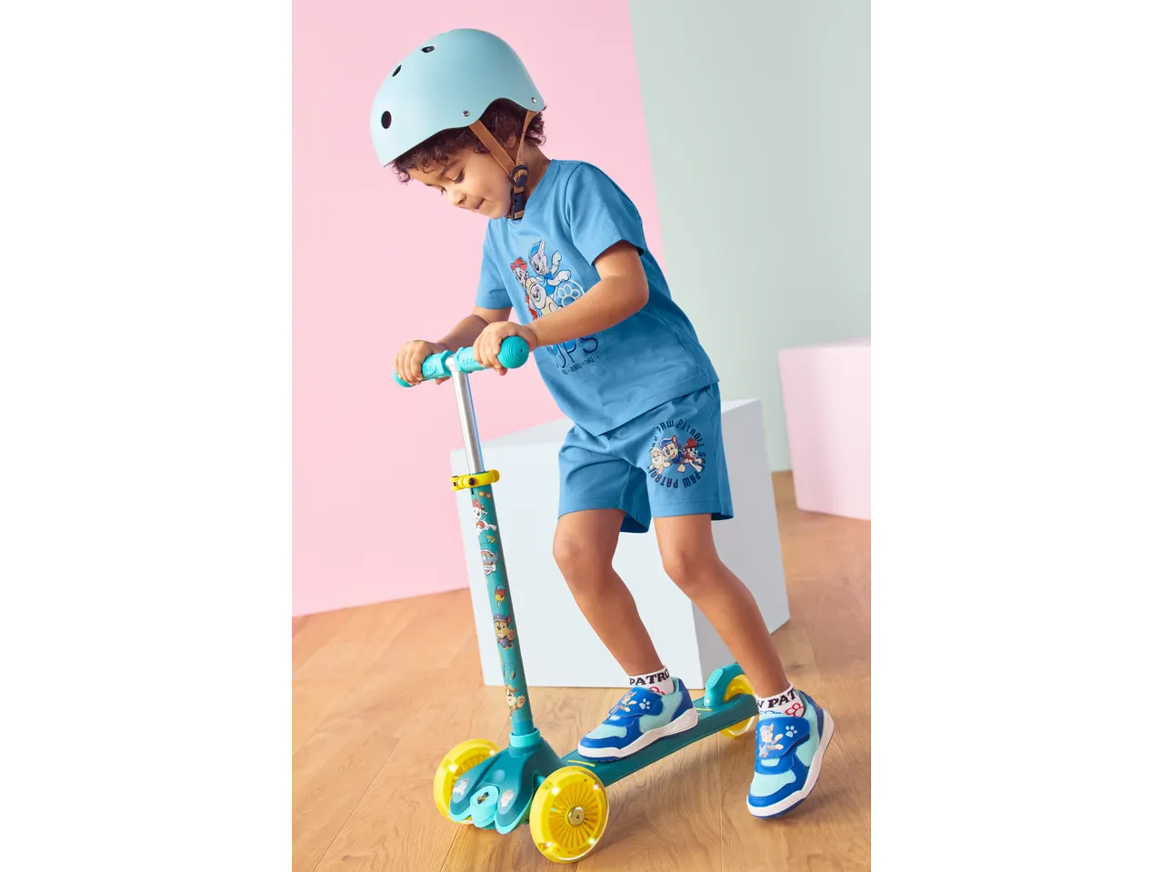 Lupilu boy in blue Paw Patrol outfit and helmet, riding a Tri-Scooter with LED wheels.