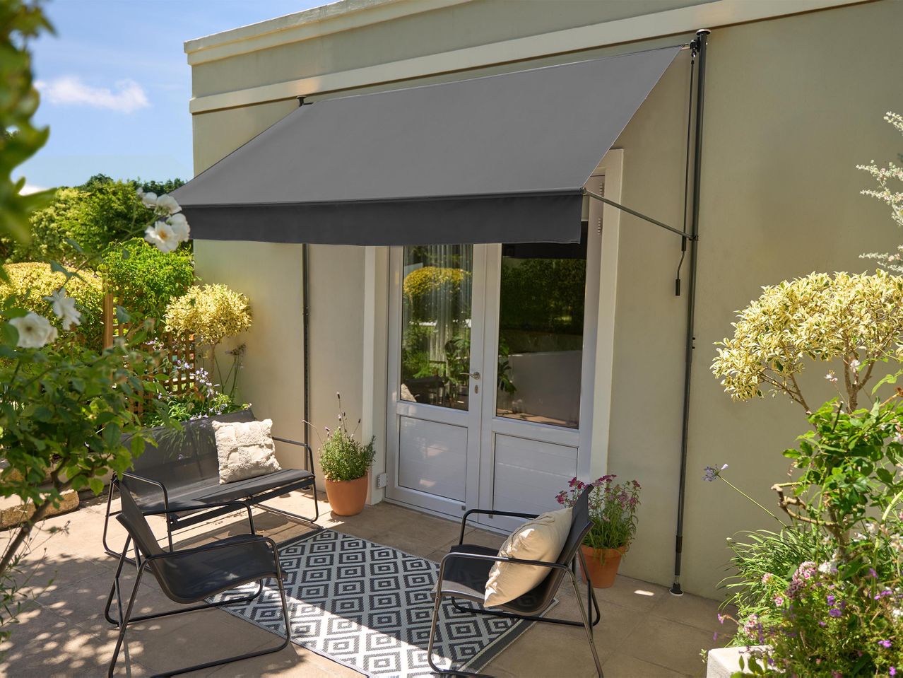 Szürke napellenző egy teraszon, két fekete székkel, párnákkal és egy mintás szőnyeggel.