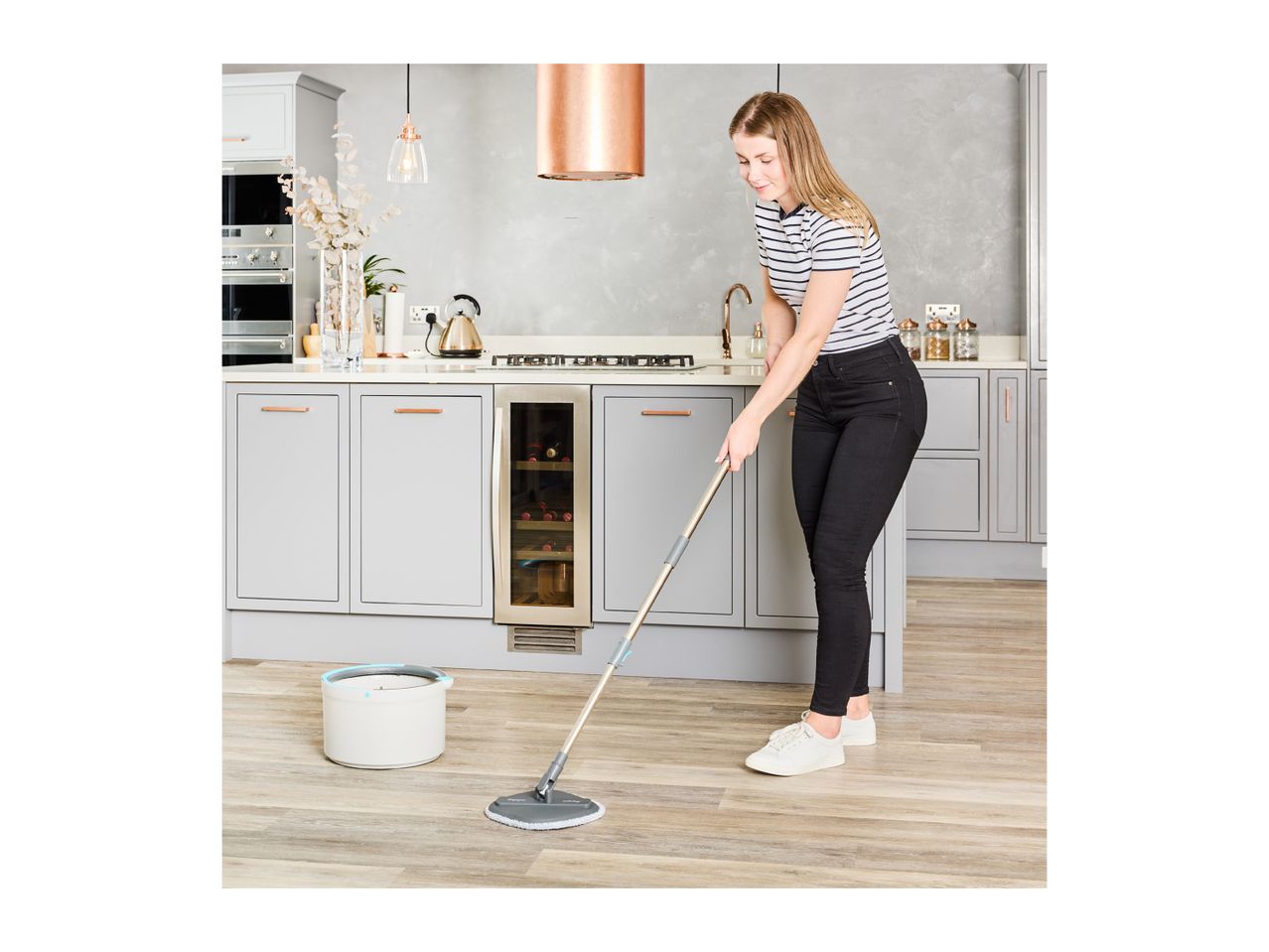 Woman mopping a modern kitchen floor with a mop and bucket.