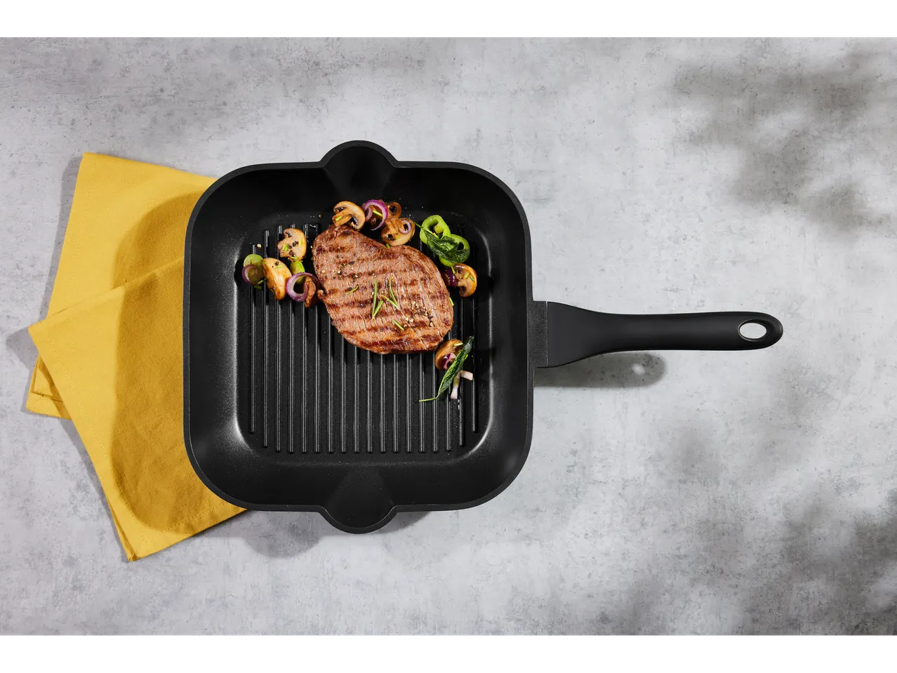 Grilled steak with vegetables in a cast aluminum pan on a yellow cloth