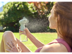 Woman using a handheld fan with water spray outdoors.