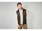 Homem com colete acolchoado preto Livergy e camisola bege, a sorrir.
