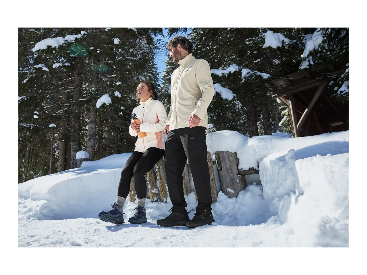 A man and a woman in warm winter clothing standing in a snowy forest.