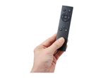 Hand holding a black remote control with various buttons, including power and navigation.