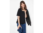 Smiling woman in a black t-shirt, blue jeans, and a black faux leather jacket over her shoulder.