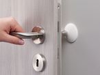 A hand opens a door fitted with a door handle and a white door stopper.