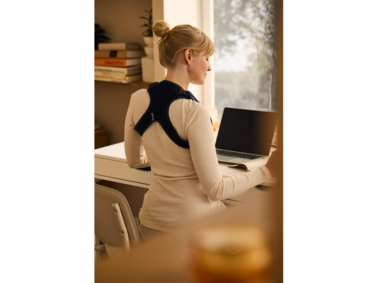 Woman wearing a posture corrector while working on a laptop at a desk.