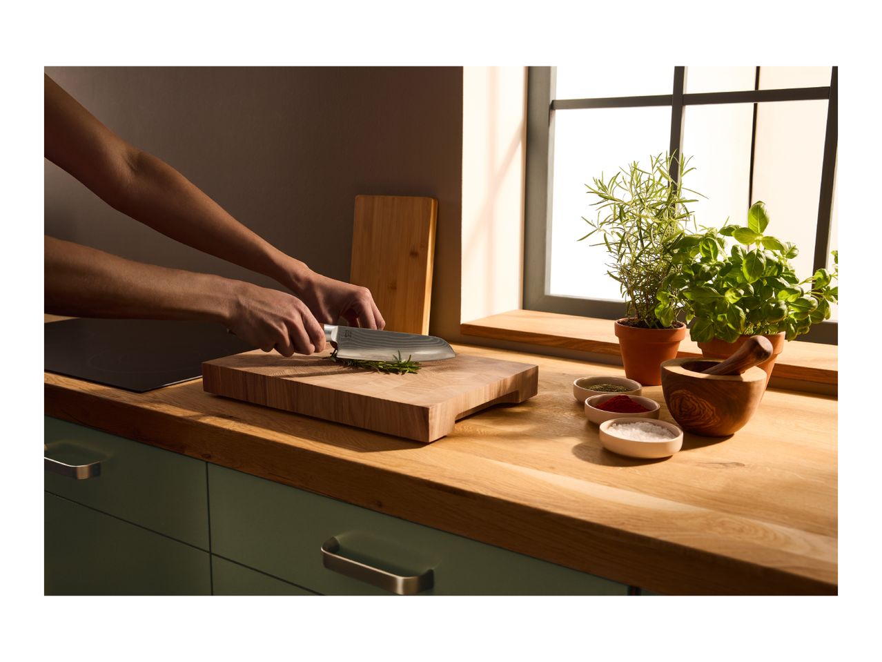 A person chopping fresh rosemary on a wooden cutting board with a chef's knife.