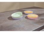 Três formas de silicone para tortas em cores pastel com tortas em uma mesa cinza.