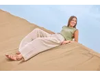 Woman in a green top and beige trousers lying on sand dunes, smiling.