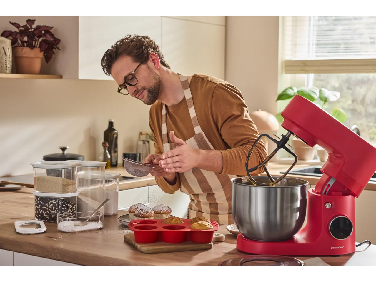 Man baking with a red SilverCrest stand mixer and silicone muffin tray.