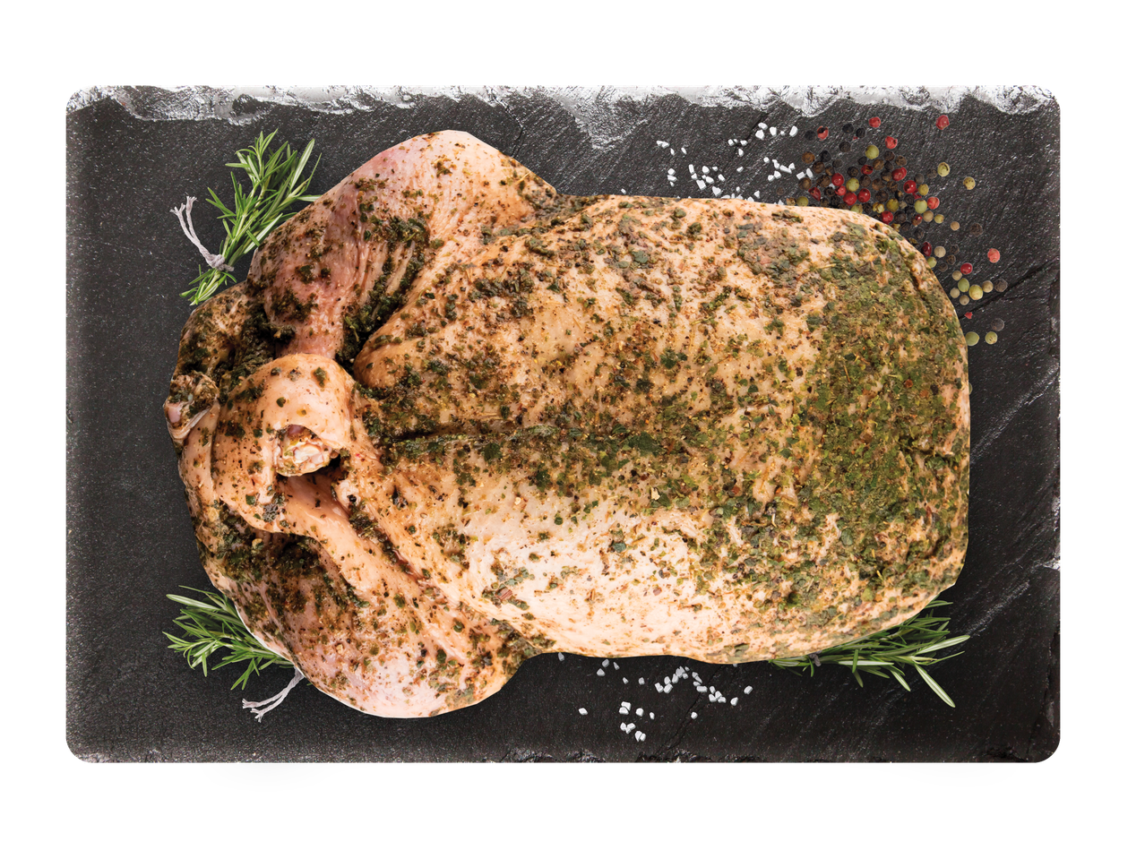 Žalia visa višta, marinuota žolelėmis, rozmarinais, druska ir pipirais ant tamsios skalūno lentos.