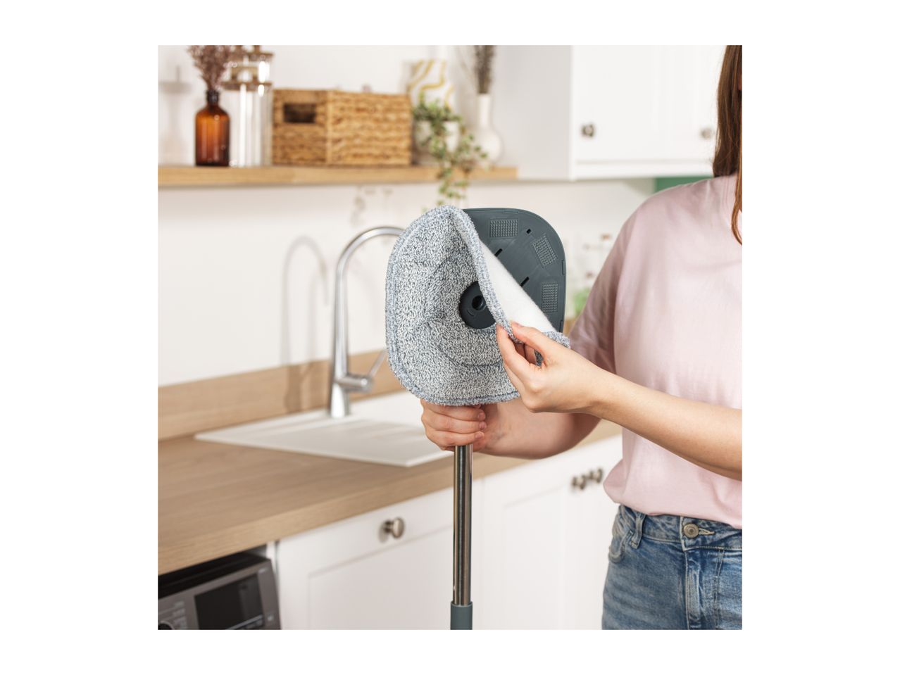 Woman attaching a microfiber mop pad to a flat mop head in a modern kitchen.