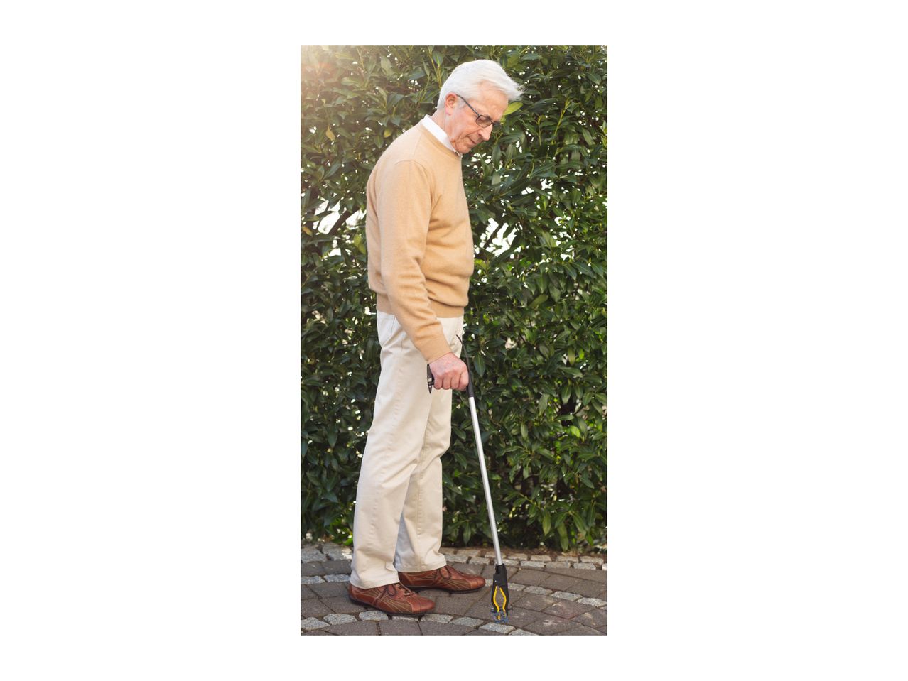 Elderly man using a grabber tool to pick something up from the ground.