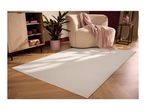 A light beige rug on a wooden floor in a living room with a cabinet, plant, and armchair.