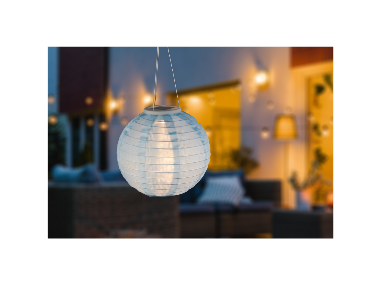 Plava papirna lampa sa solarnom svetlošću visi u pozadini prijatne bašte.