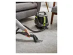 A person cleaning a stain on a gray carpet with a Daewoo carpet cleaner.