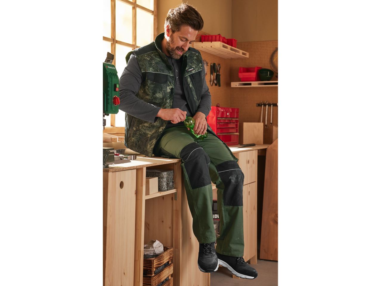 Man in PARKSIDE PERFORMANCE® work trousers and vest, sitting on a workbench.