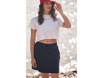 Model purtând un tricou alb și o fustă sport bleumarin lângă mare.