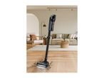 Cordless stick vacuum cleaner cleaning dirt on a wooden floor in a living room