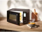 Silvercrest microwave with an open door and a bowl of hot soup on a wooden countertop.
