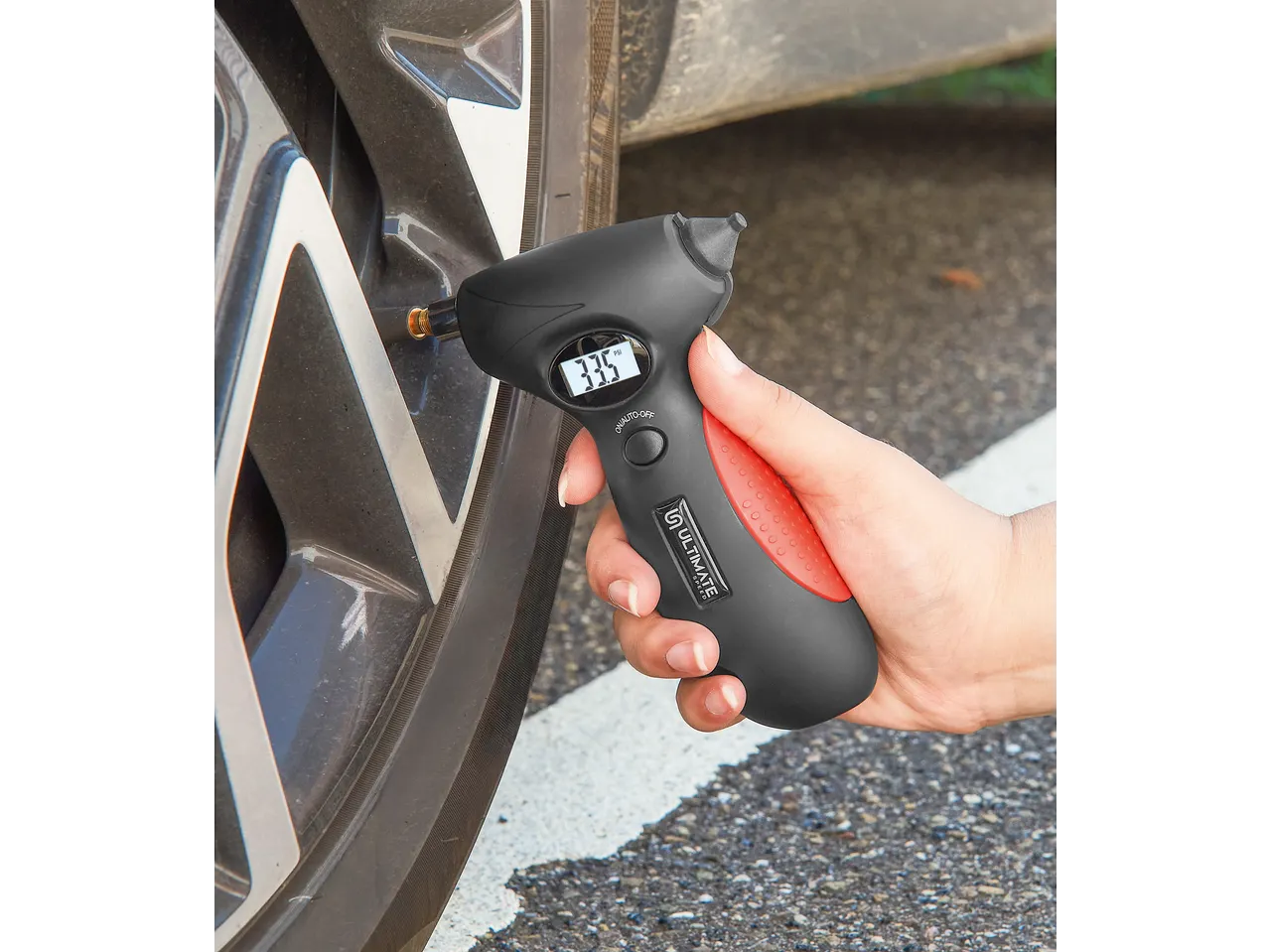 Hand holding a digital tire pressure gauge, displaying 33.5 PSI, on a car tire.