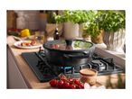 Black pot with glass lid on a gas hob, cooking cherry tomatoes and herbs.