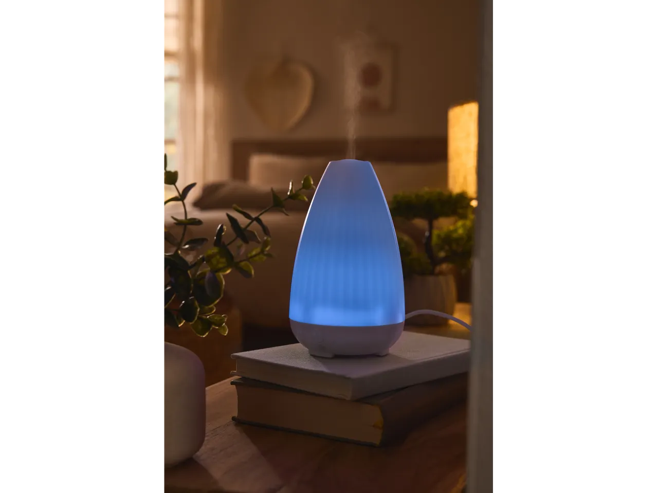 Difuzor de aromă cu ultrasunete LIVARNO home cu lumină albastră pe cărți lângă pat.