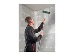 Man sanding a wall with a long-handled sanding tool in a room under renovation.