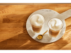 Dois copos de café latte com espuma de leite numa tábua de mármore.
