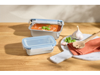 Two stainless steel food containers, one with tomato soup, on a wooden table with garlic and basil.