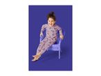 A laughing child in unicorn pajamas sits in a purple chair against a purple background.