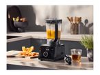 A black soup maker blender on a kitchen counter next to fresh ingredients and a measuring cup.