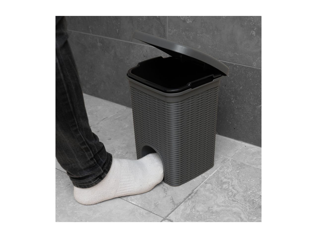A person's foot in a white sock opening a grey pedal bin with a textured design.
