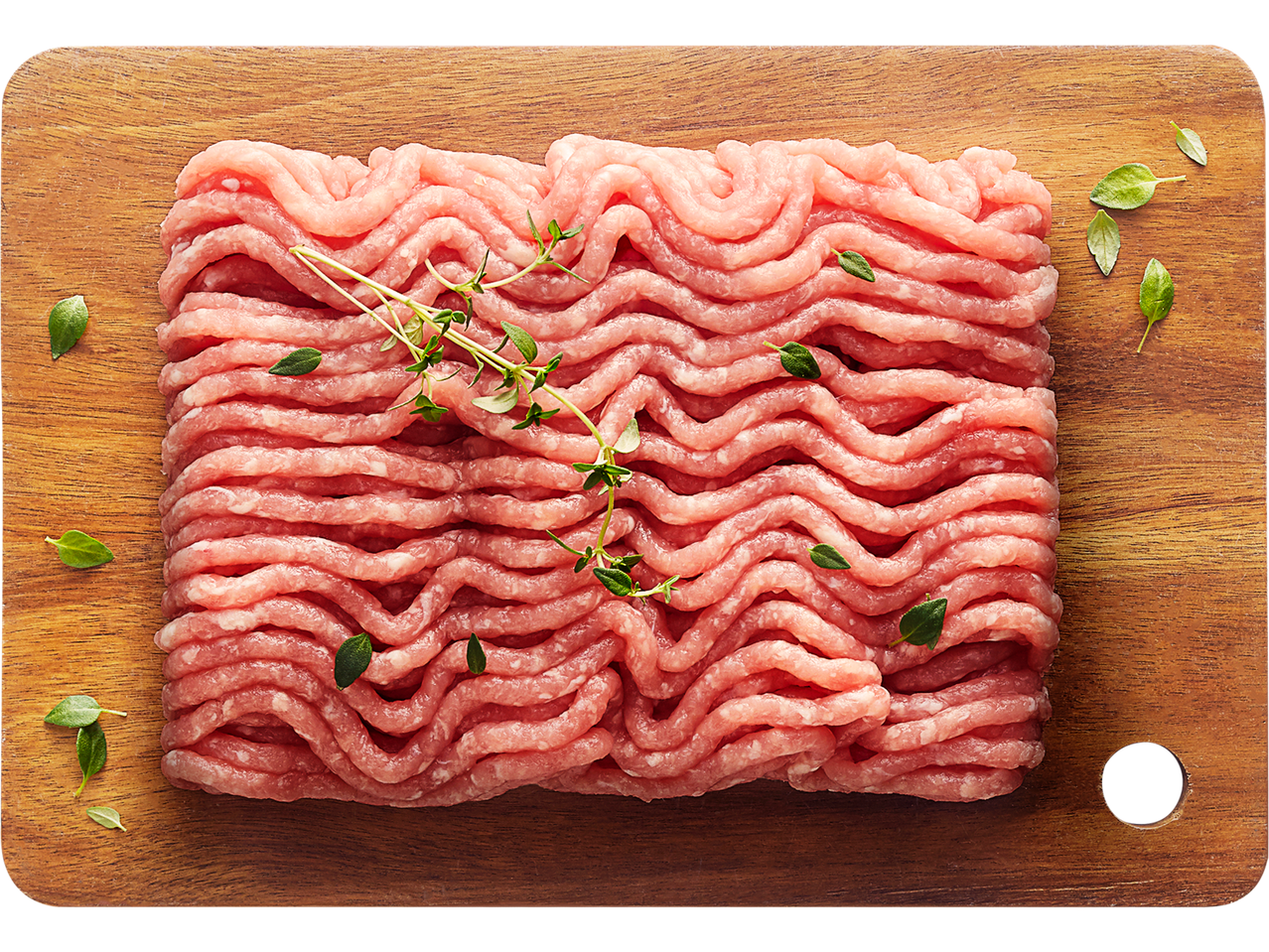 Šviežias smulkintas kiaulienos kumpis ant medinės pjaustymo lentos su čiobreliais ir žolelėmis