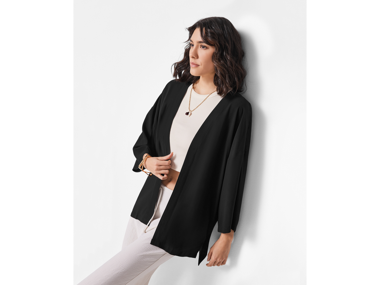 Modella con kimono corto nero e pantaloni beige.