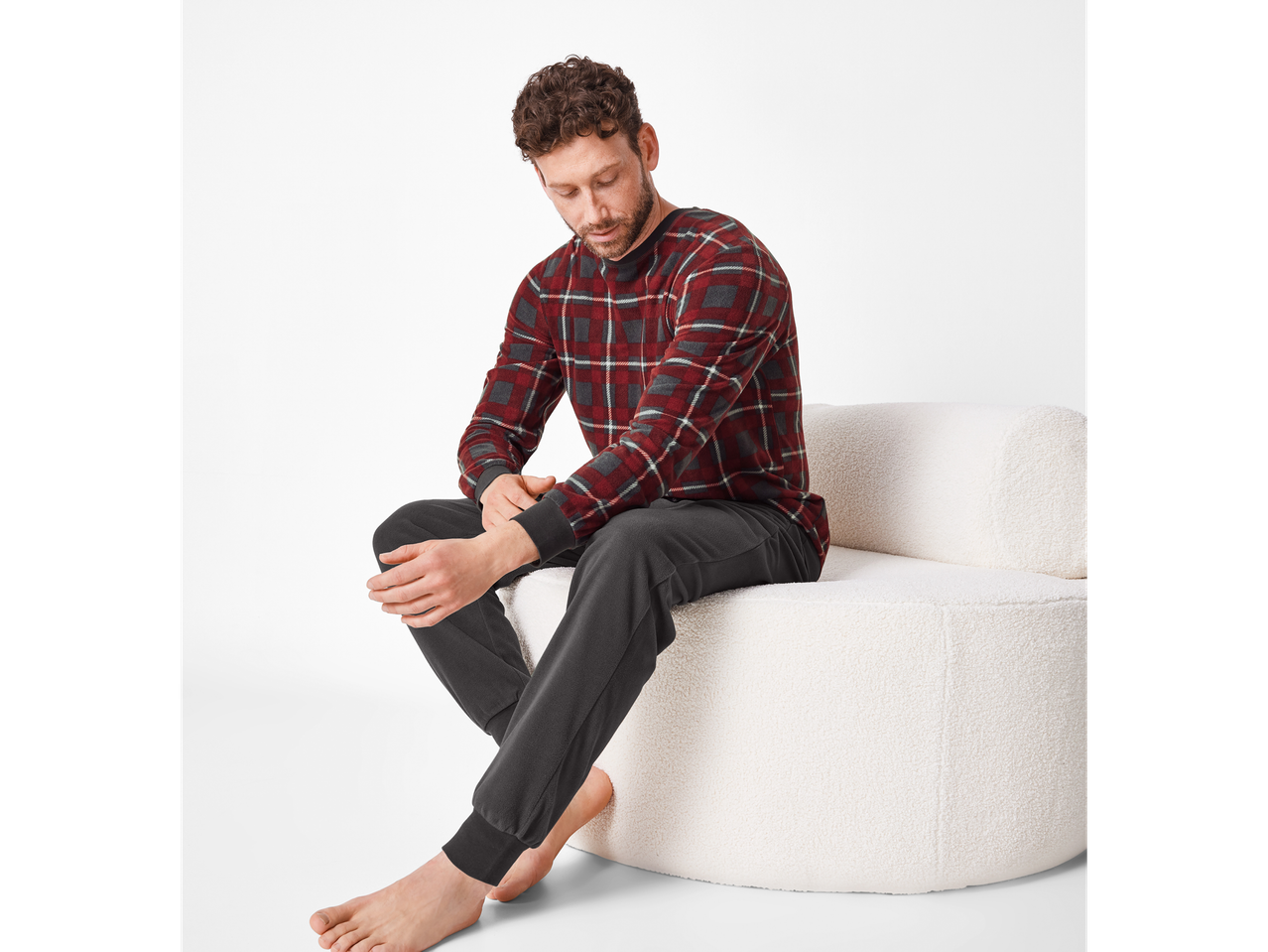 Man in red and grey plaid pajamas sitting on a white textured chair.