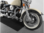A cream and black motorcycle with chrome details and white sidewall tires sits on a black mat.