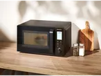 A black microwave on a wooden counter with spices and a cutting board.