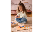 A young girl plays with a colorful wooden pattern block set on a rug.