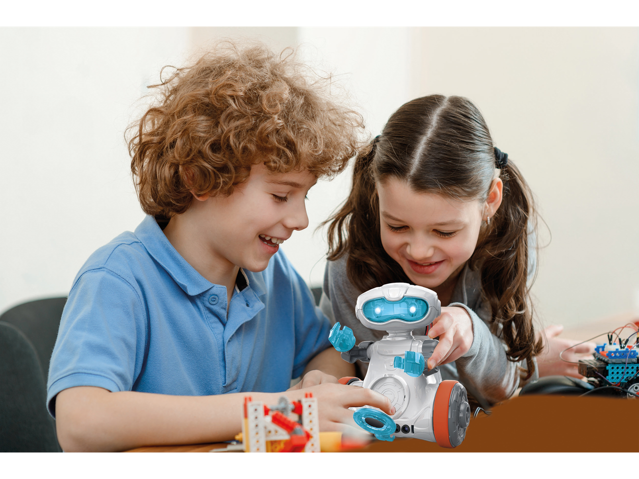Dvoje djece igra se s bijelim robotom igračkom i kockama.