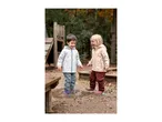 Two happy children in waterproof jackets and trousers splashing in a puddle.