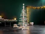 Albero di Natale in legno con decorazioni, luci e regali in una stanza verde scuro.