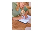 Woman tracing a drawing on a light pad with a pencil, on a wooden table.