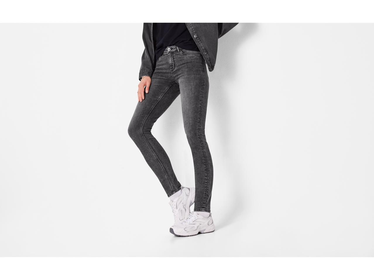 Esmara ženske tamnosive traperice, nošene s bijelim sportskim cipelama.