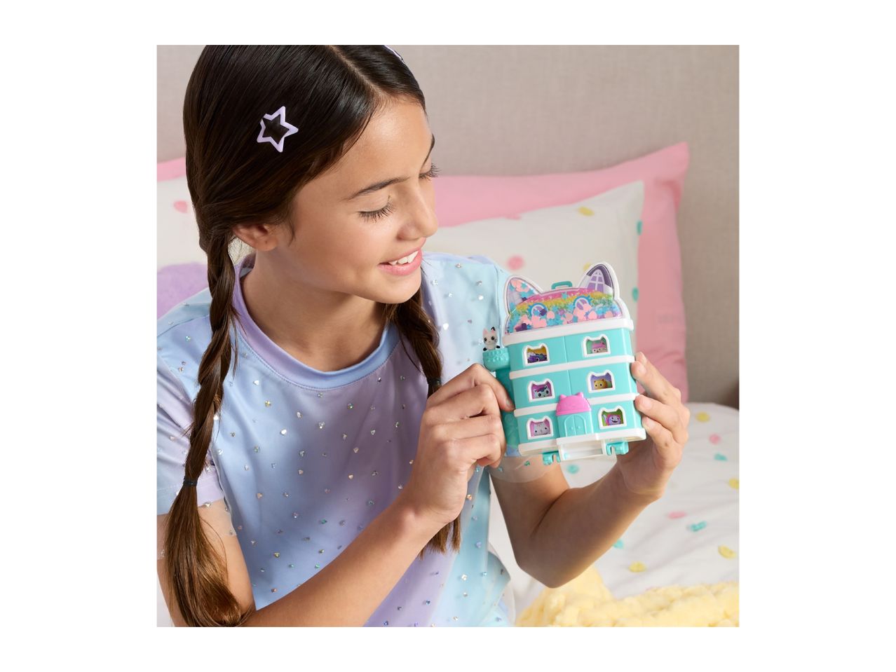 A girl holding a teal cat-themed toy house with multiple levels and small figures.