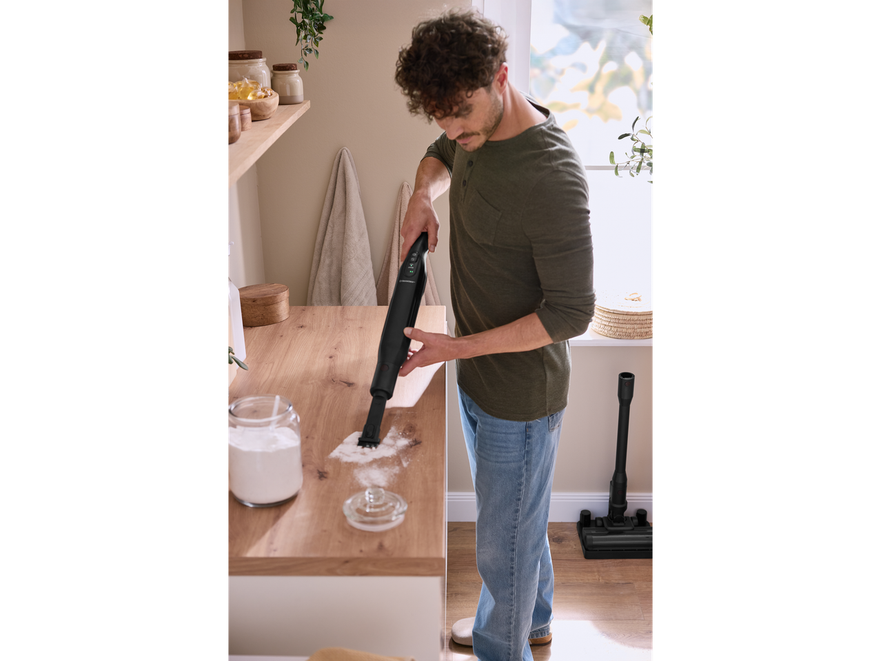 Muškarac usisava brašno sa stola Silvercrest® 2 u 1 bežičnim usisavačem.